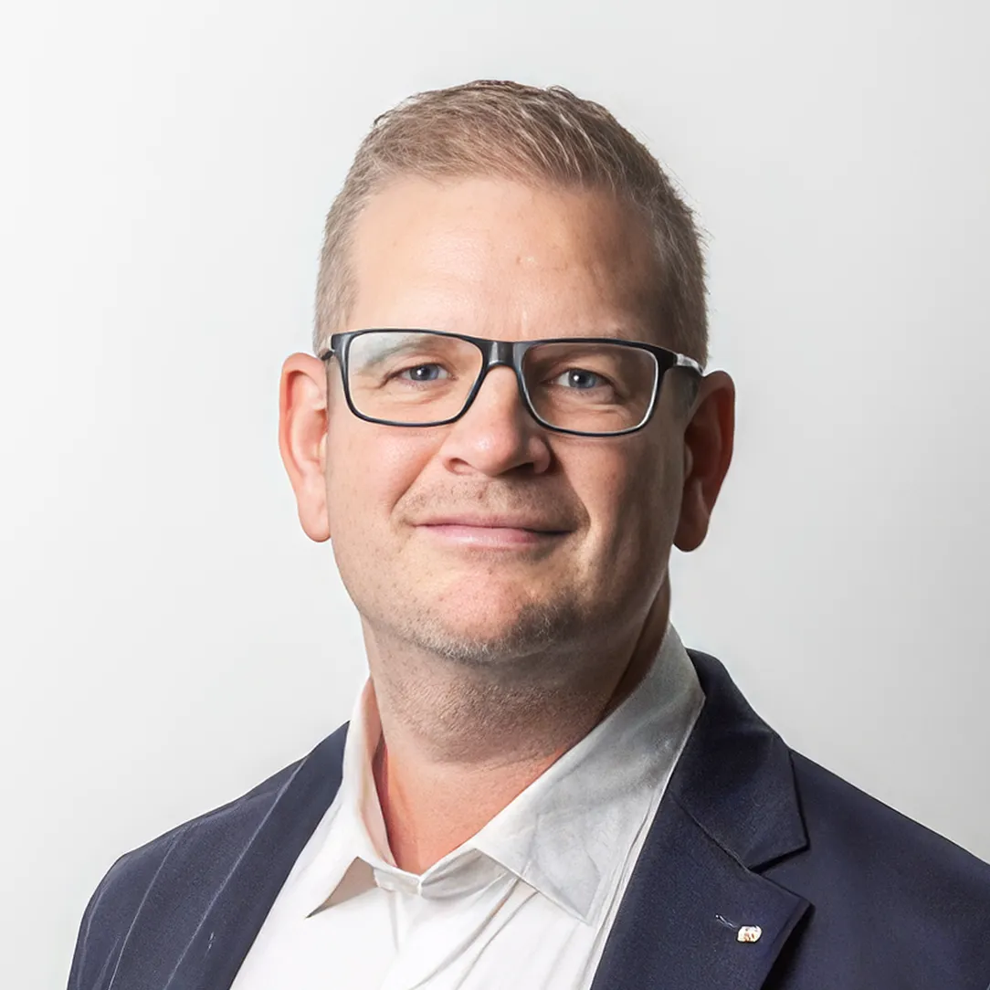 Portrait of Mark Gorholt wearing glasses and a dark blazer on a neutral studio background